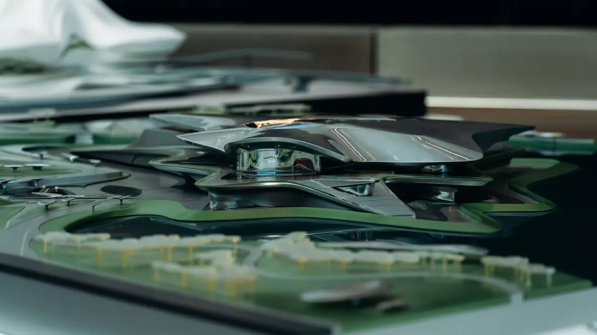 Close-up of a sleek architectural model with a metallic building form set among a green landscape